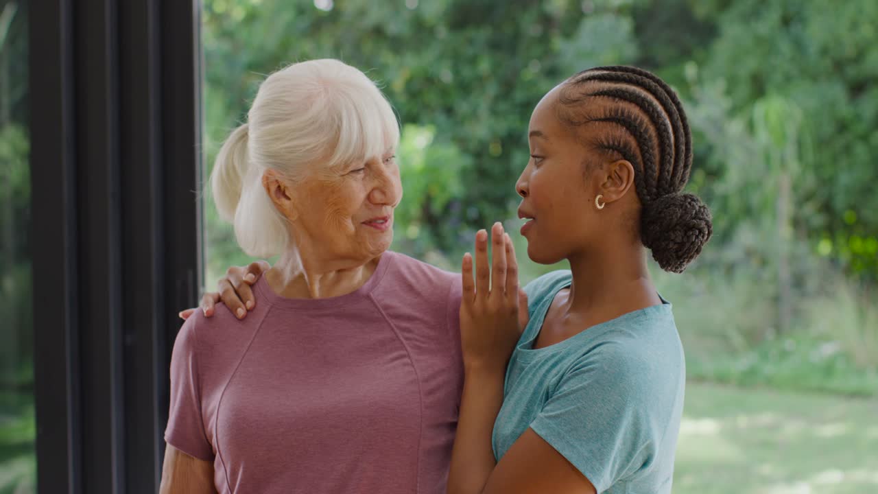 Female relatives, African woman placing hands on senior, laughing warmly at door, mauve teal shirts