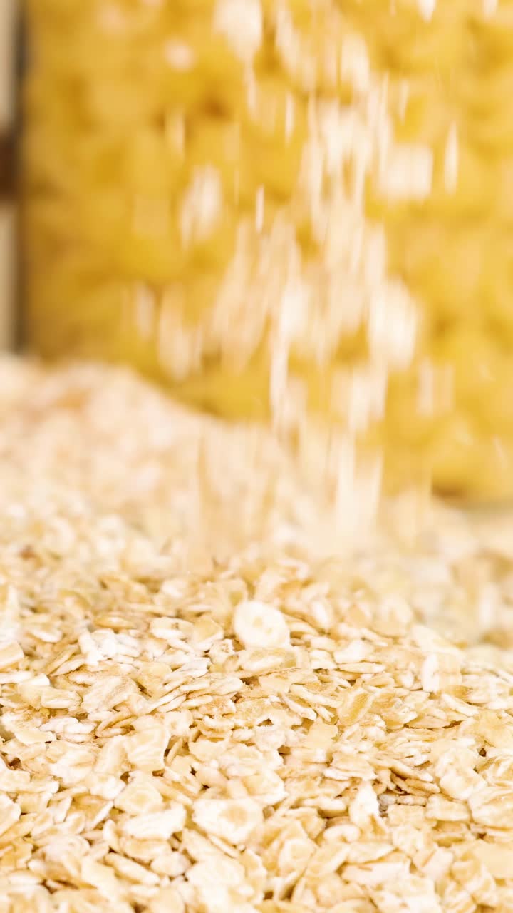 Fiocchi d'avena cadono a cascata da un contenitore, formando un mucchio su uno sfondo giallo vivace. L'illuminazione brillante esalta la consistenza.