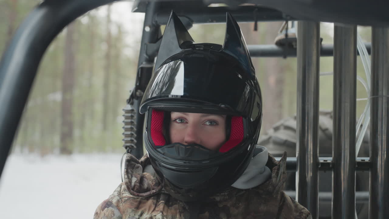 Atv rider snowy forest helmet closeup, driver scans trail from utv cabin, glossy black helmet with red liner, breath fog in cold air, camouflage jacket, steel rollcage frame, focused eyes, prestart