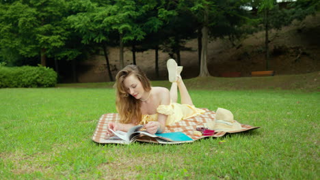 Impresionante-Mujer-Vestida-De-Amarillo-Acostada-Boca-Abajo-En-El-Parque-Hojeando-Un-Libro