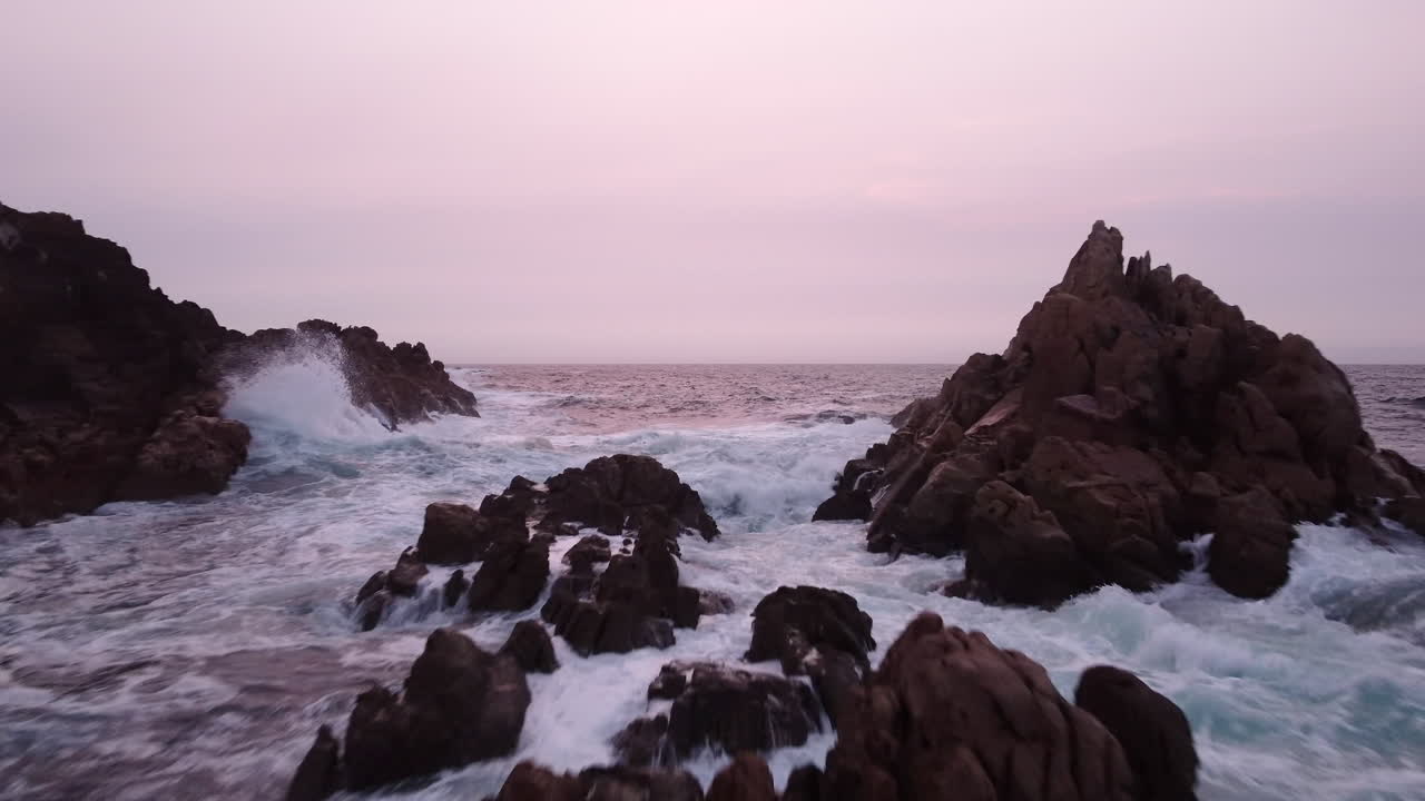 Cielo rosa al tramonto e costa rocciosa e frastagliata, sorvolo aereo sul mare