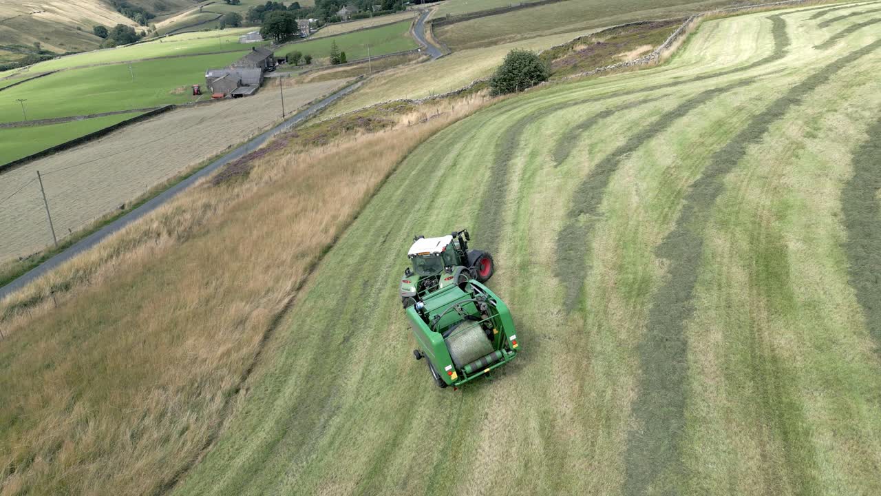 트랙터가 들판을 가로질러 운전하고 잘린 짚으로 베일을 만드는 항공 영상