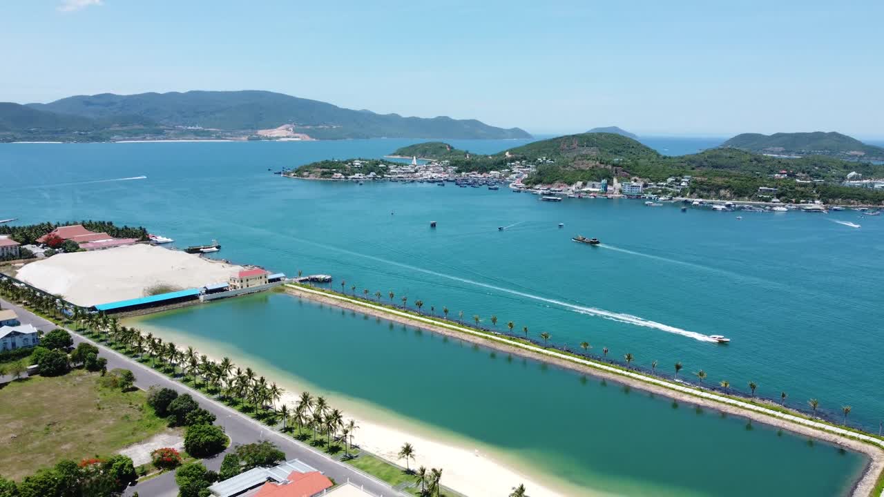Veduta aerea con drone di un canale costiero vicino all'isola di Hon Tre con barche che attraversano il mare blu lungo la costa di Nha Trang e colline tropicali in Vietnam