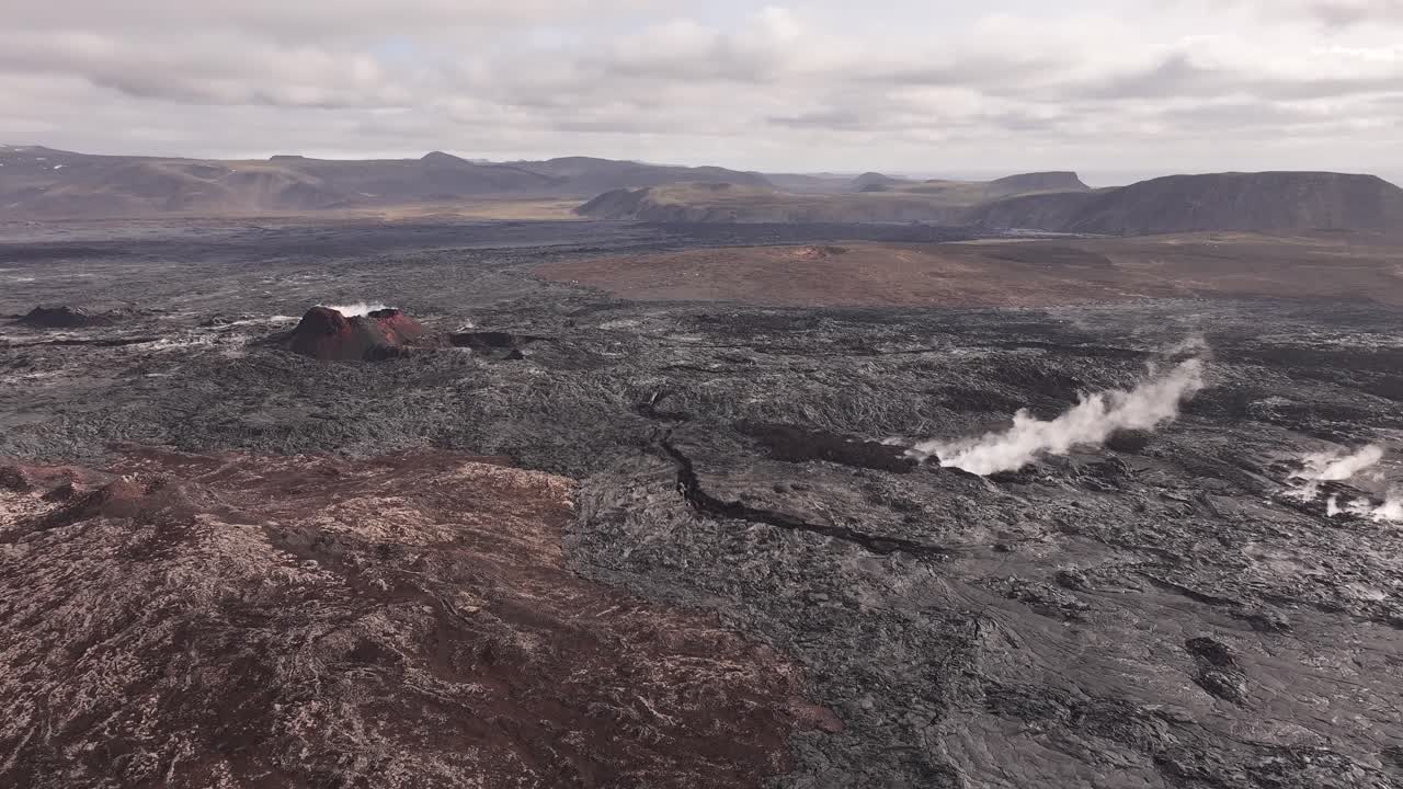 Aerial view of a volcanic crater and steaming fissure in a rugged lava field in Iceland.