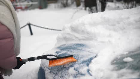 woman removing snow from a car in winter