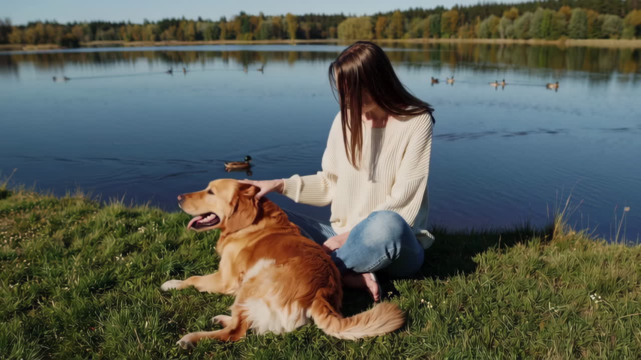 A woman petting her golden retriever dog by a lake