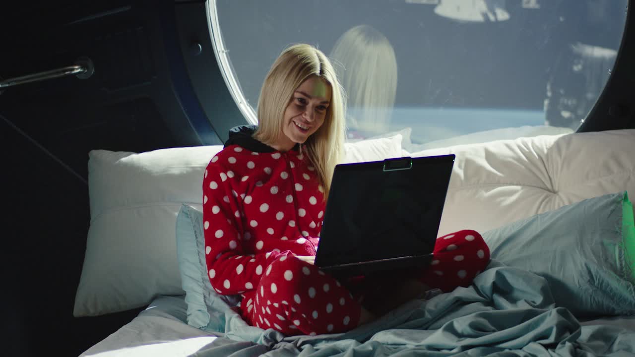 Woman in pajamas working on laptop/pad in space cabin