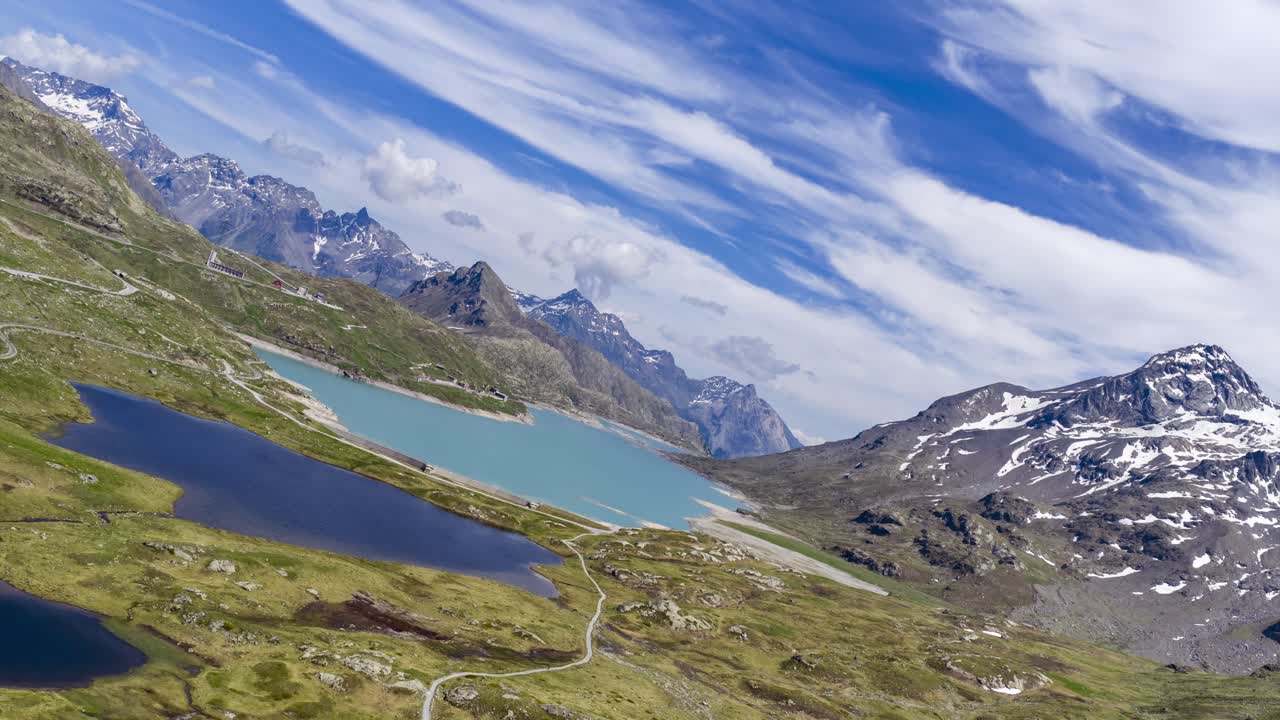 Hyperlapse aereo del Passo del Bernina che mostra laghi glaciali, pendii verdi e montagne innevate sotto un cielo dinamico. Aereo, hyperlapse.