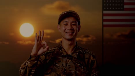 close up of asian man soldier smiling and showing okay gesture to camera while standing with flag of the united states, sunset time