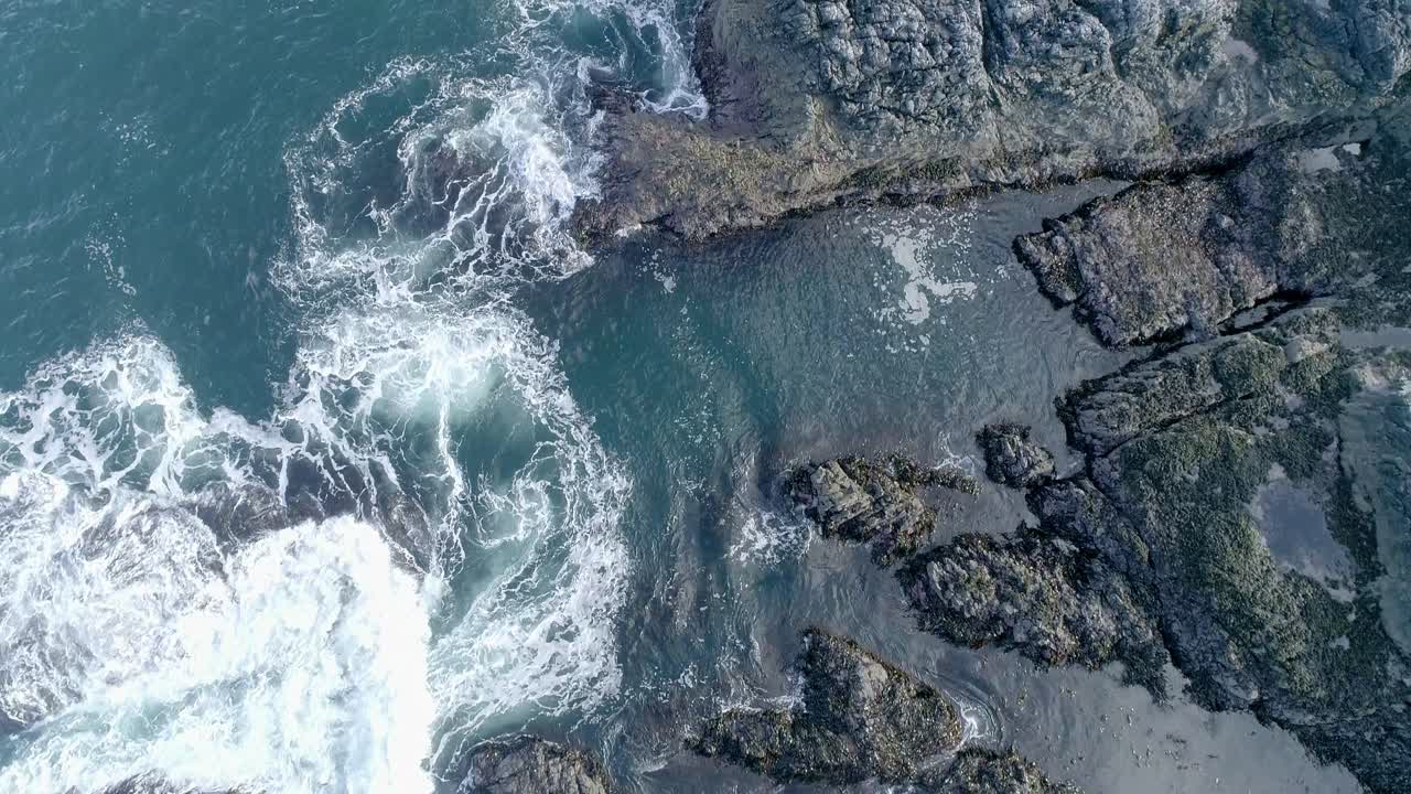 las aguas turbulentas de las mareas ondulan sobre la costa rocosa baja, los charcos y las rocas escarpadas son visibles contra el mar turquesa poco profundo
