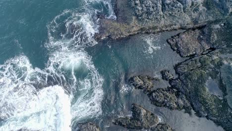 rough swirling tidal waters wave over low lying rocky coastline, rockpools and craggy rocks are visible against the shallow turquoise sea