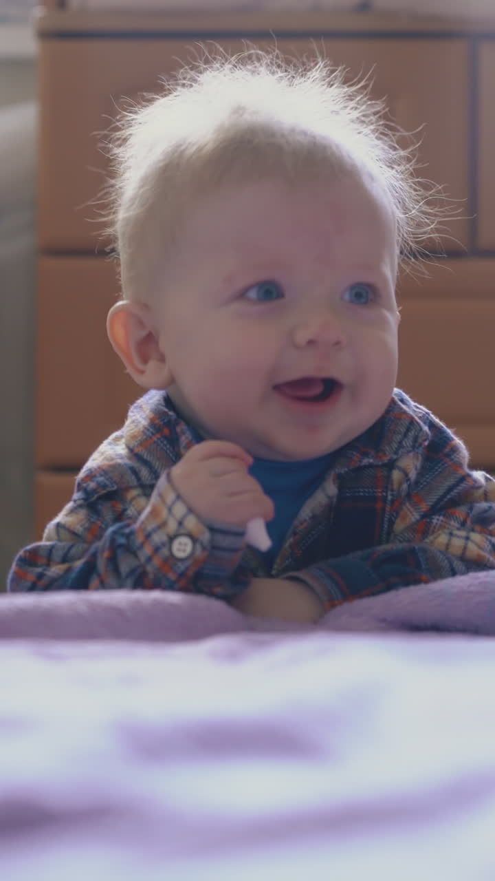funny little boy in warm shirt plays with plastic tube of medical aspirator at bed with pink plaid in room
