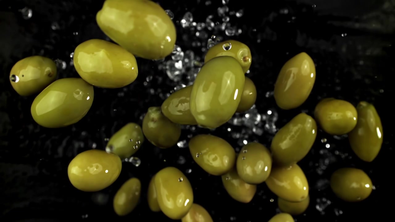 Super slow motion di olive verdi con gocce d'acqua su sfondo nero.