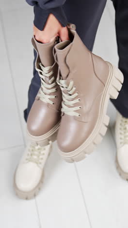 female model wearing loose pants and white tractor sole boots holding another pair of beige boots in hands. view from above. white floor backdrop. vertical video