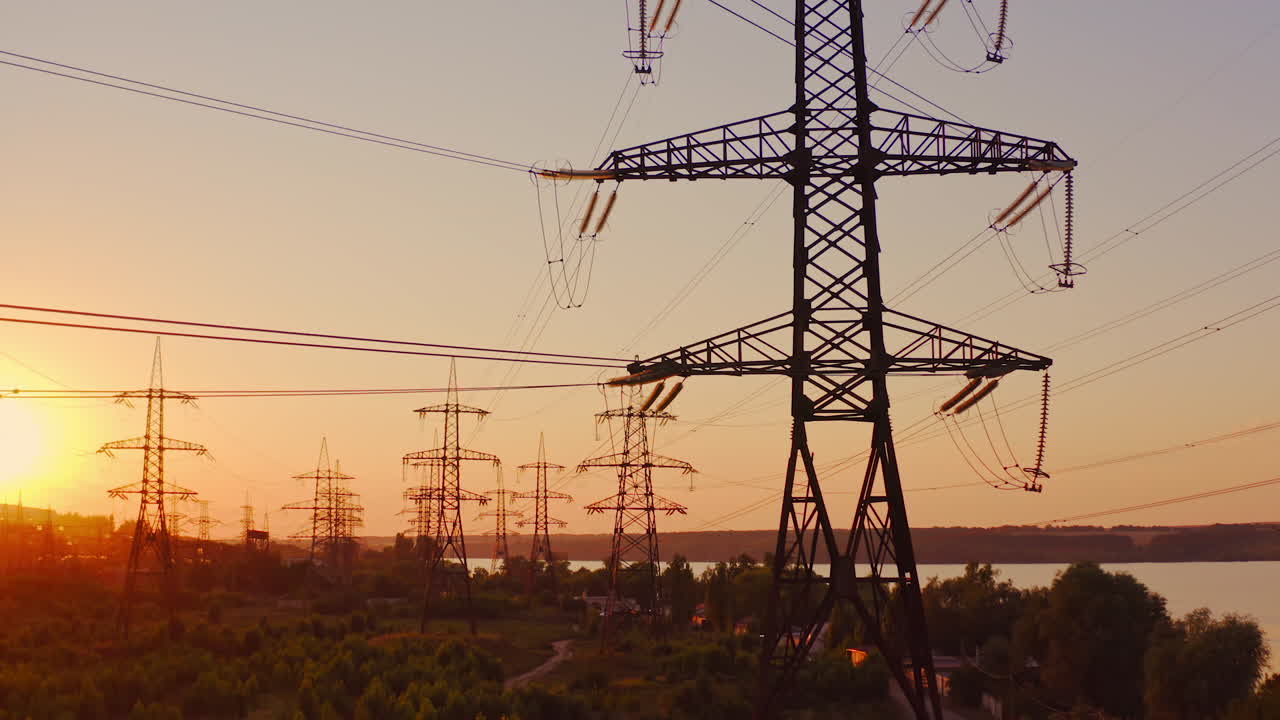 Transmission lines near the river. High-voltage electric towers at sunset. Distribution and supply of electricity. Camera rising up.