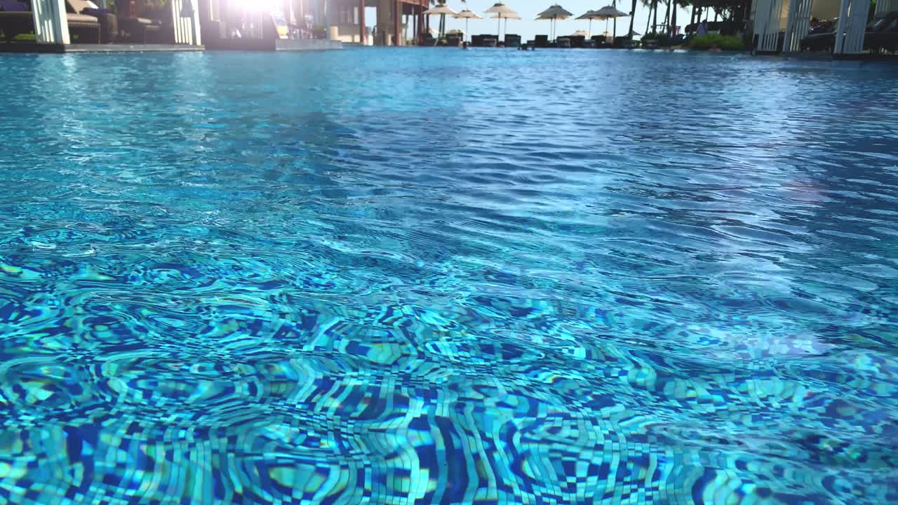Cool refreshing water in a swimming pool with silhouette of people and shade umbrellas in the background