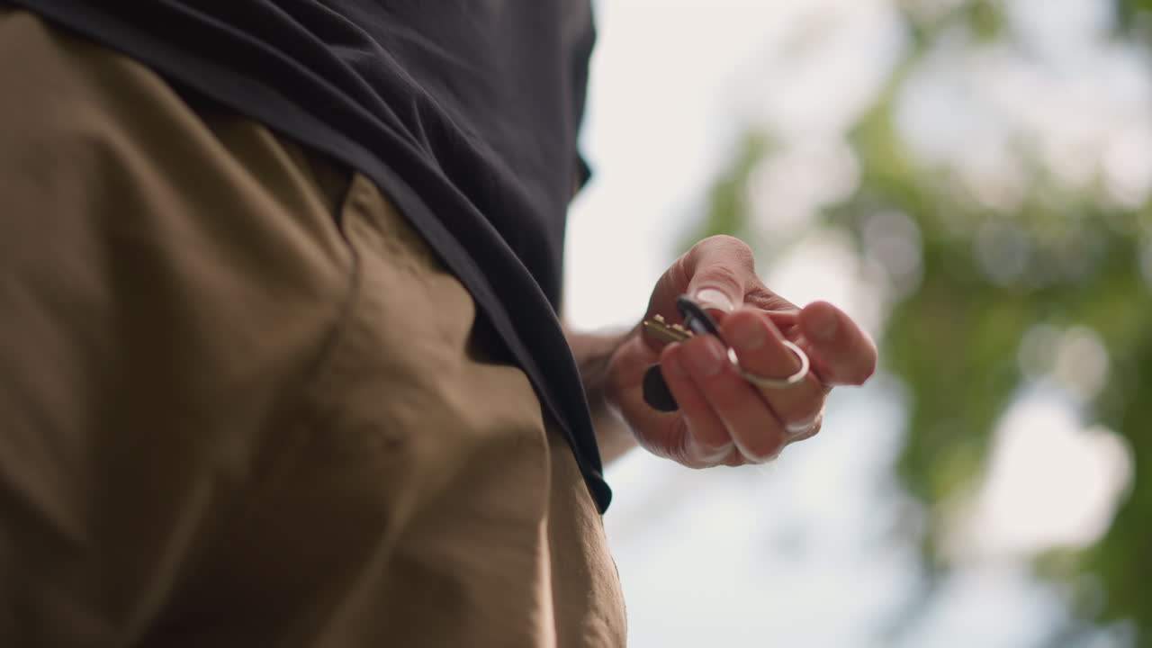 Man Placing Keys In Pocket During Outdoor Activity, Unposed Shot Of Individual Tucking Keys Into Pocket At Park, Relaxed Scene Where Man Secures Keys In Khaki Pants Near Exercise Equipment