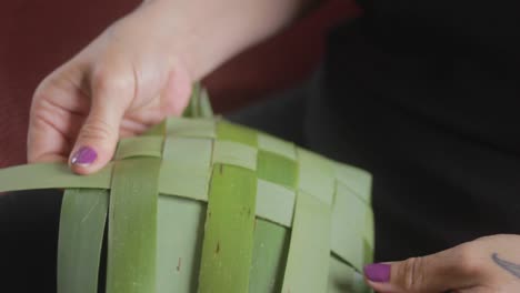 closeup in slow motion of a woman weaving plants to make a basket in a traditional maori way