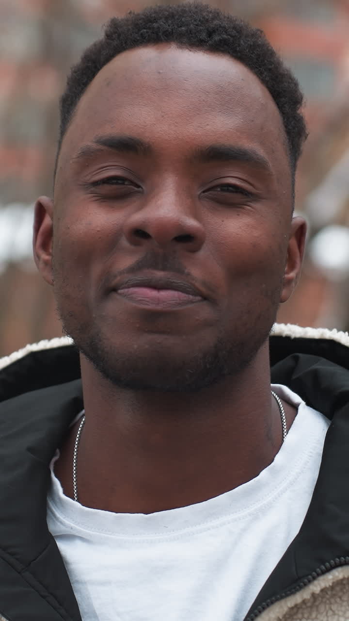 celebridad negra con peinado afro con capucha de invierno, dando una cálida sonrisa confiada al aire libre con árboles y edificios en el fondo, irradiando energía positiva y estilo