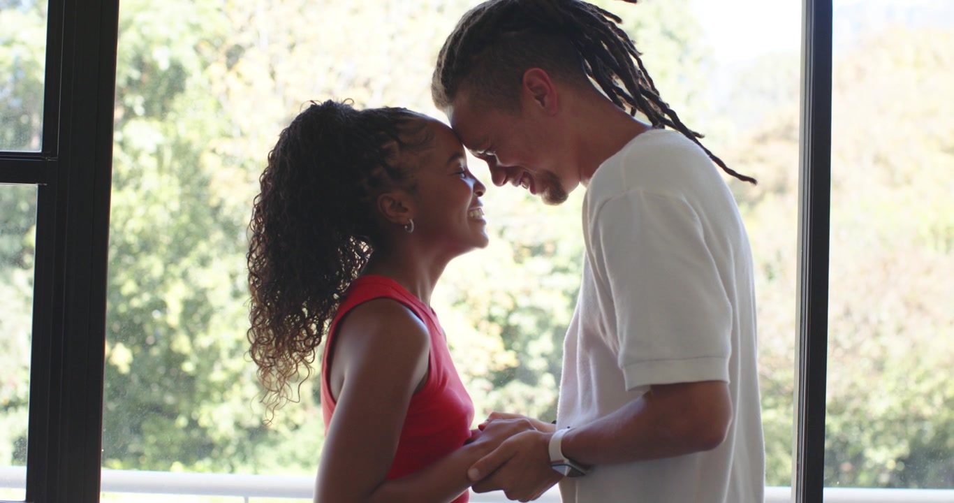 African American couple grasping hands expressing affection in doorway, woman in red smiling