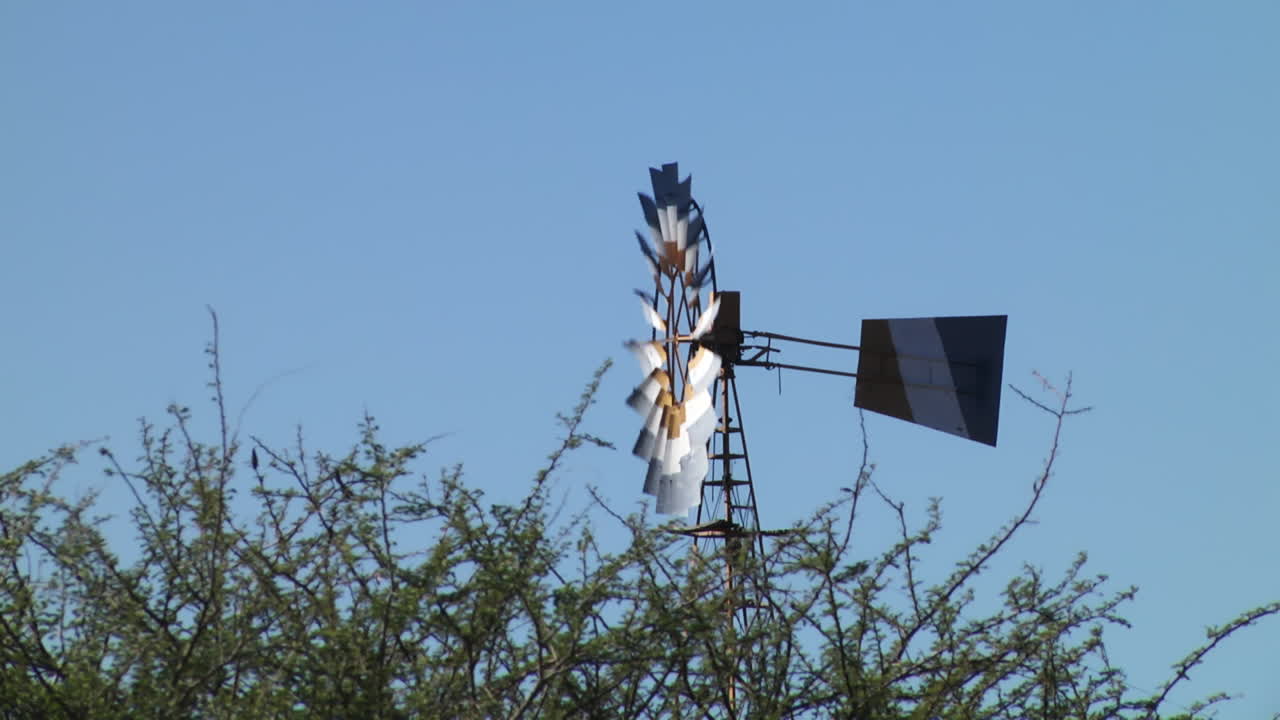 Side View Of Vintage Spinning Country Windmill Against Blue Skies. Locked Off