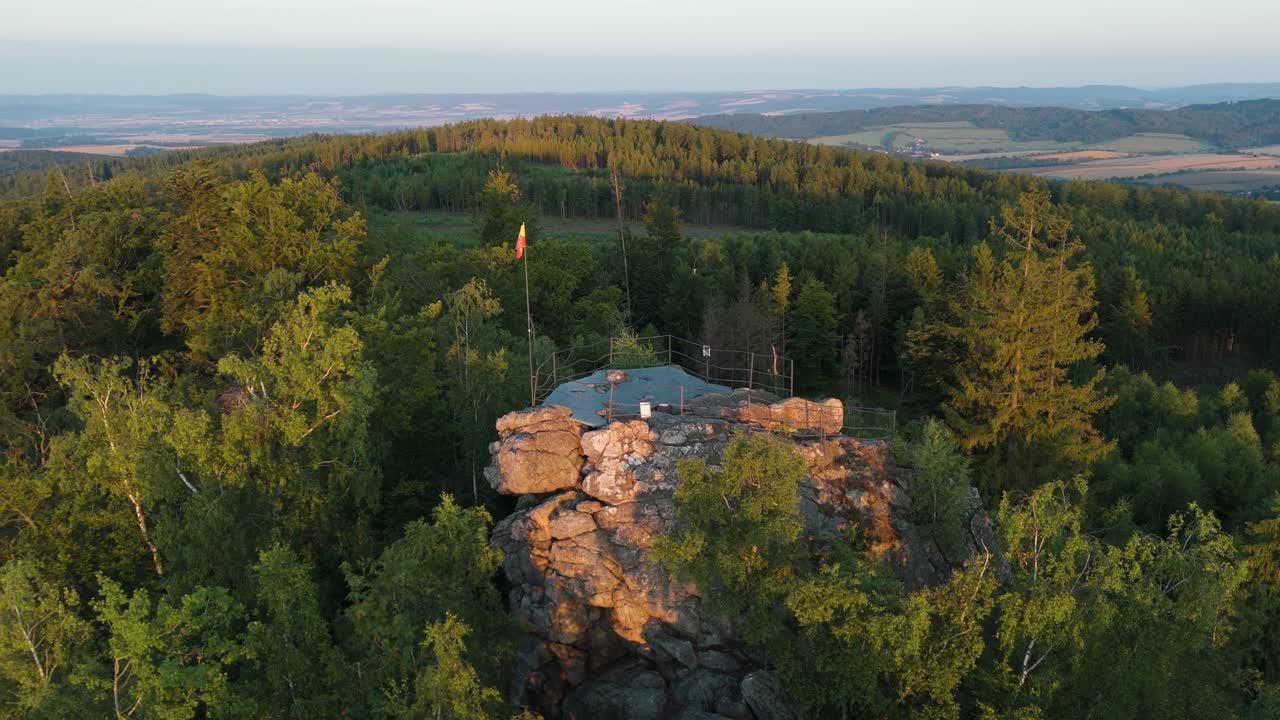 Flying around a rock formation within woods with a lookout spot lit by morning sunlight