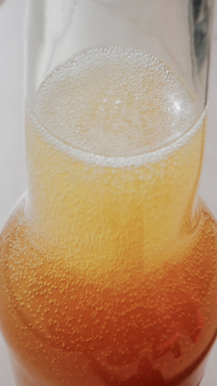 Close up view of fizzy drink with golden bubbles rising inside a glass. Vertical