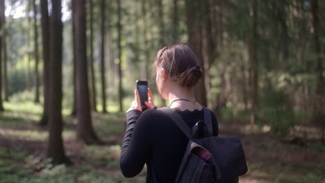 una joven con una mochila captura la belleza del bosque en su teléfono