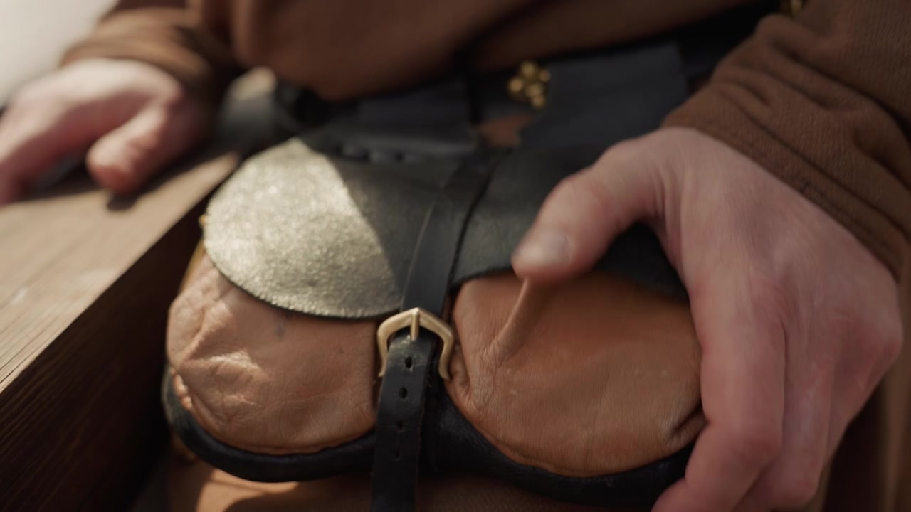 Primo piano delle mani che fissano una borsa di pelle con fibbia e patta, mostrando una presa attenta, un movimento di pressione e un posizionamento preciso in una luce calda e rustica per conservazione artigianale, artigianato o uso del prodotto
