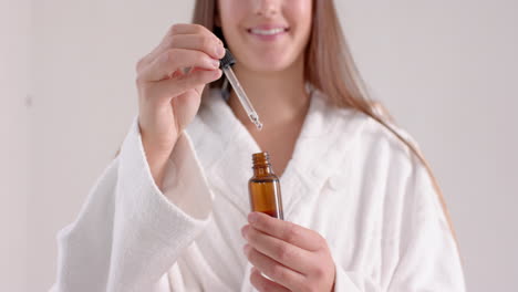 applying serum with dropper, woman in bathrobe enjoying spa treatment at home