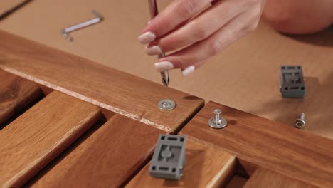 a hand uses a screwdriver to assemble wooden furniture, focusing on precision and detail in a well-lit environment