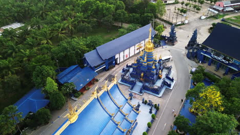 tilt down establishing aerial of vibrant blue buddhist temple with ornate sculptures and reflective tiles, chiang rai thailand