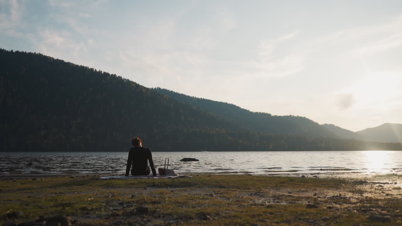 una mujer gira la cabeza para aliviar el dolor descansando en la orilla del río después de la puesta del sol. una mujer con una canasta de comida disfruta de un picnic sola en la belleza intacta de la naturaleza al crepúsculo en la noche de otoño