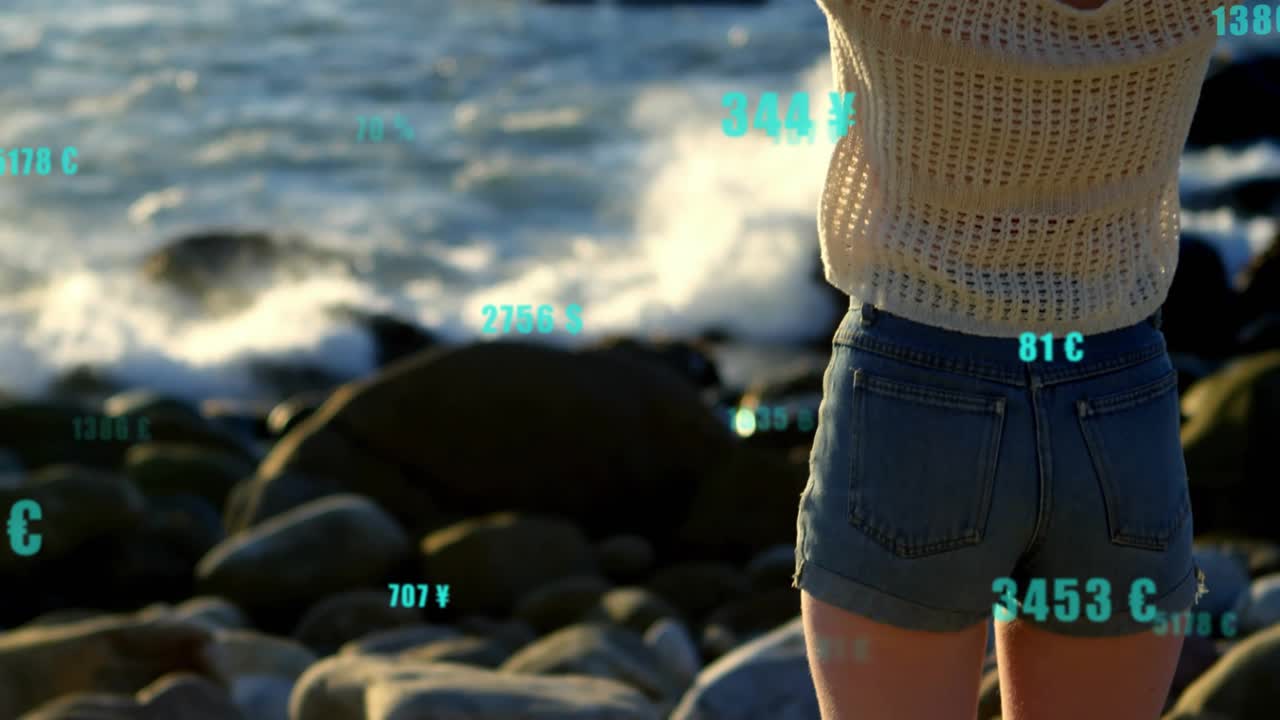 Telecamera che si sposta verso l'alto rivelando una donna che si aggiusta i capelli su una costa rocciosa con dati di valuta fluttuanti.
