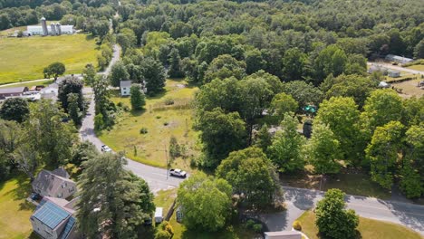 a shot of 3 cars driving down a road near a forest with houses and land around them