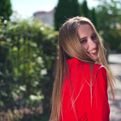 backside view of a beautiful woman outdoors. long-haired girl walking along the street in summer. lovely female in red dress turns her head and smiles on camera.