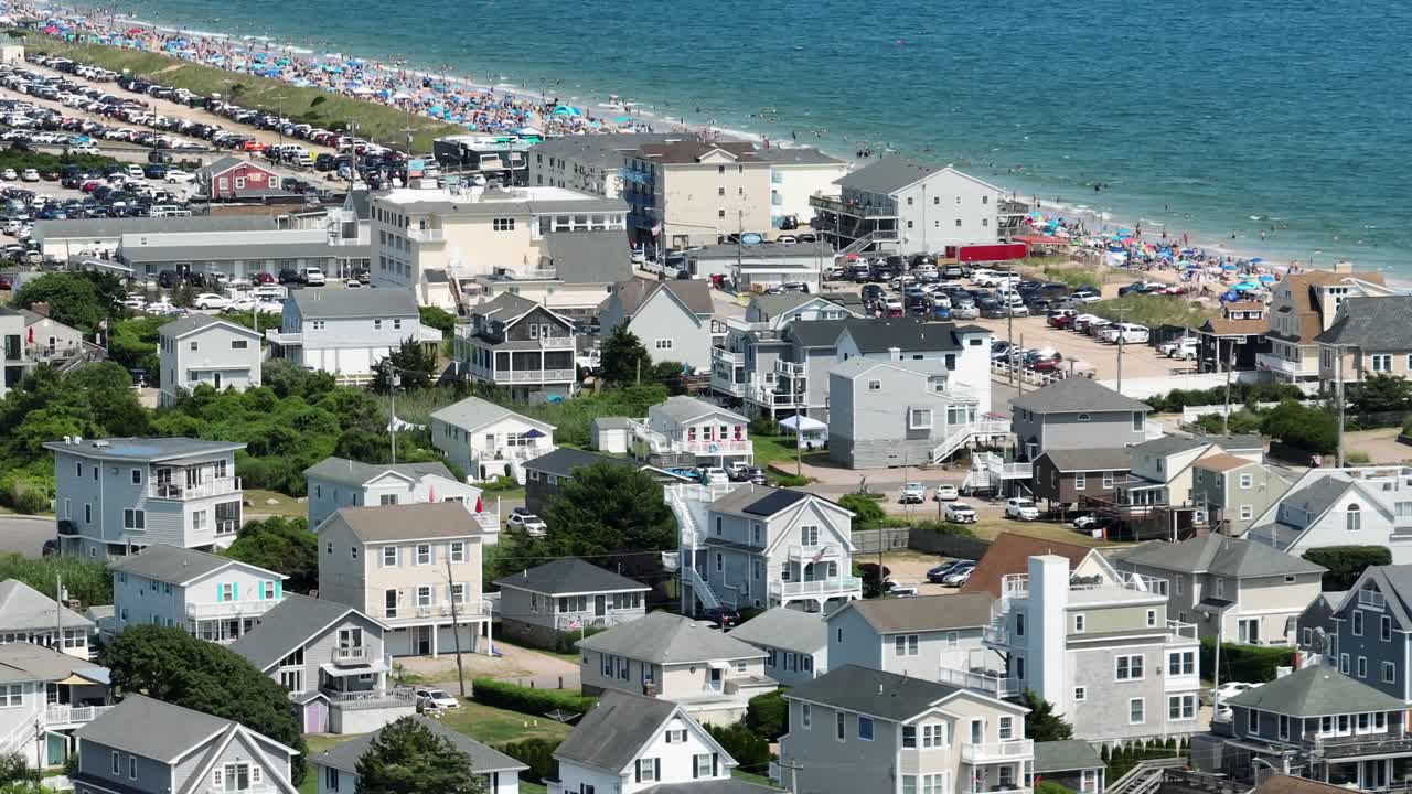 Aerial view of Misquamicut Beach, Rhode Island, showing seaside houses, busy beachfront, parked cars and colorful umbrellas along the Atlantic Ocean. Wide shot. Sunny summer day in USA