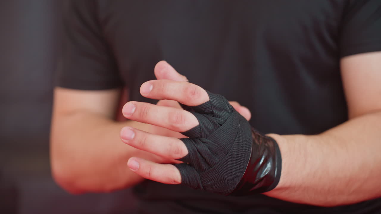 Boxer carefully wraps hands with black bandages, securing wrists and knuckles for strength, endurance, and protection before training session, demonstrating preparation, and focus inside combat sports