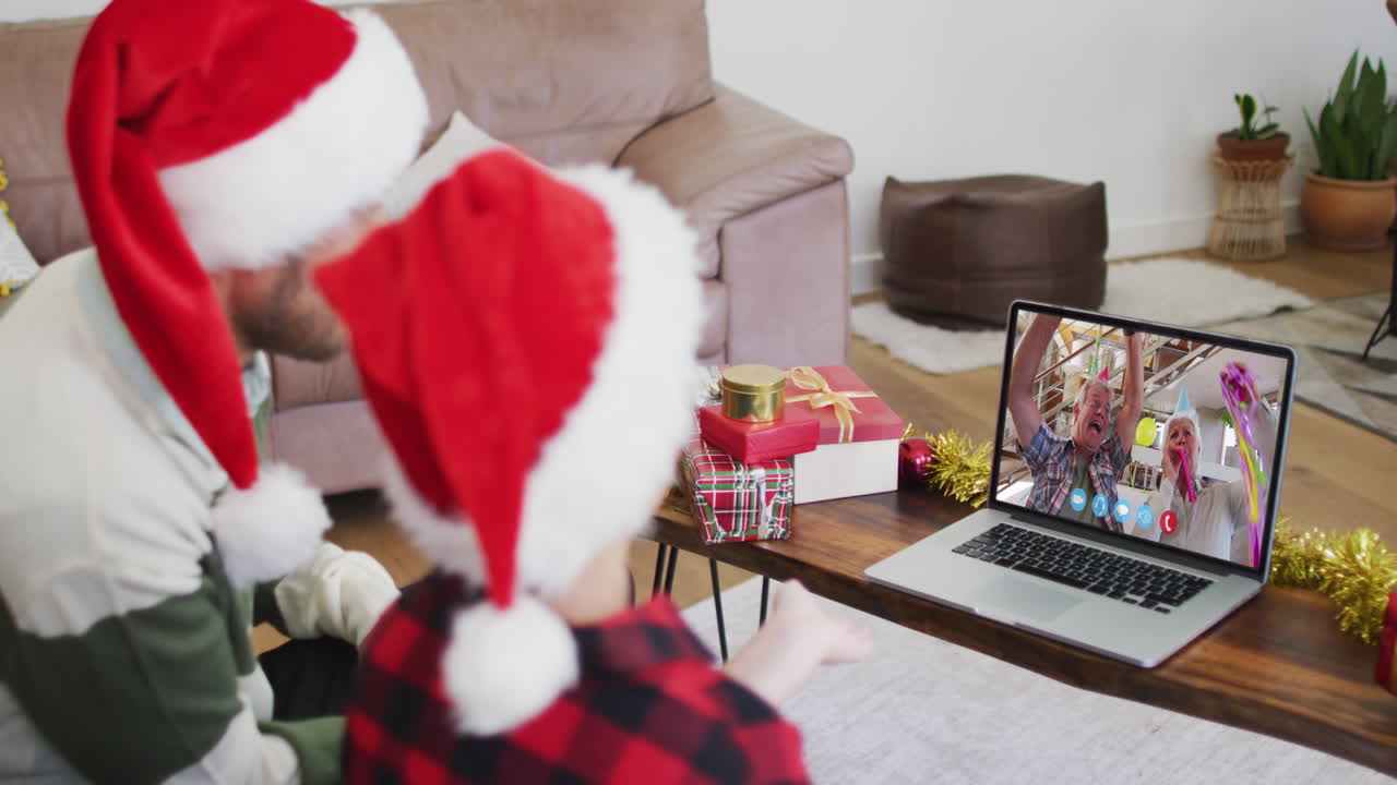 padre y hijo caucásicos usando sombreros de santa en una videochat portátil durante la navidad en casa