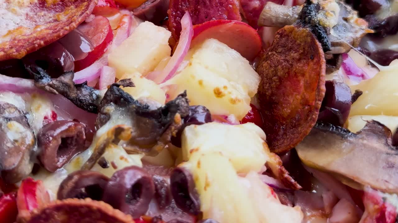 A detailed view of pizza toppings including pineapple, olives, mushrooms, and pepperoni slices.