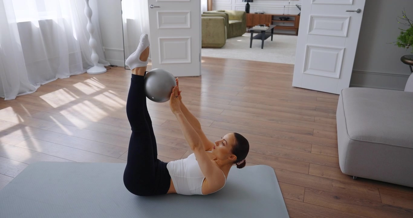 Giovane donna che esegue sollevamenti delle gambe Pilates con una piccola palla a casa