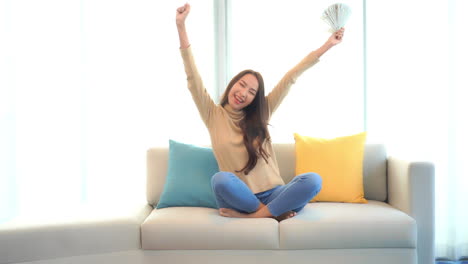 slow-motion of attractive asian girl winning prize lottery, exited face expression, she is holding a stack of dollar notes, slow-motion mid-shot