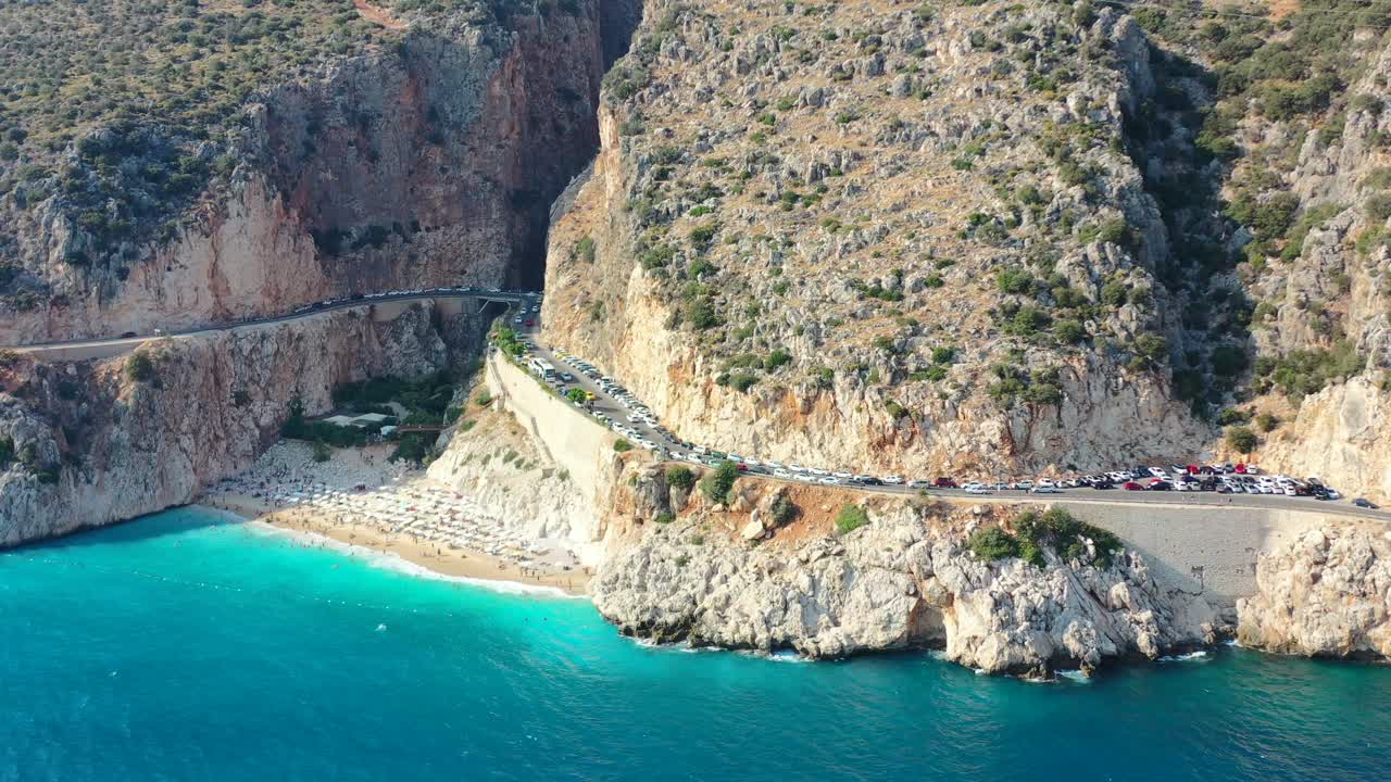 aerial drone panning out revealing a coastal road at Kaputas Beach in Kas Turkey on a sunny afternoon day during summer as tourists relax along the Mediterranean Sea in the summer surrounded by cliffs