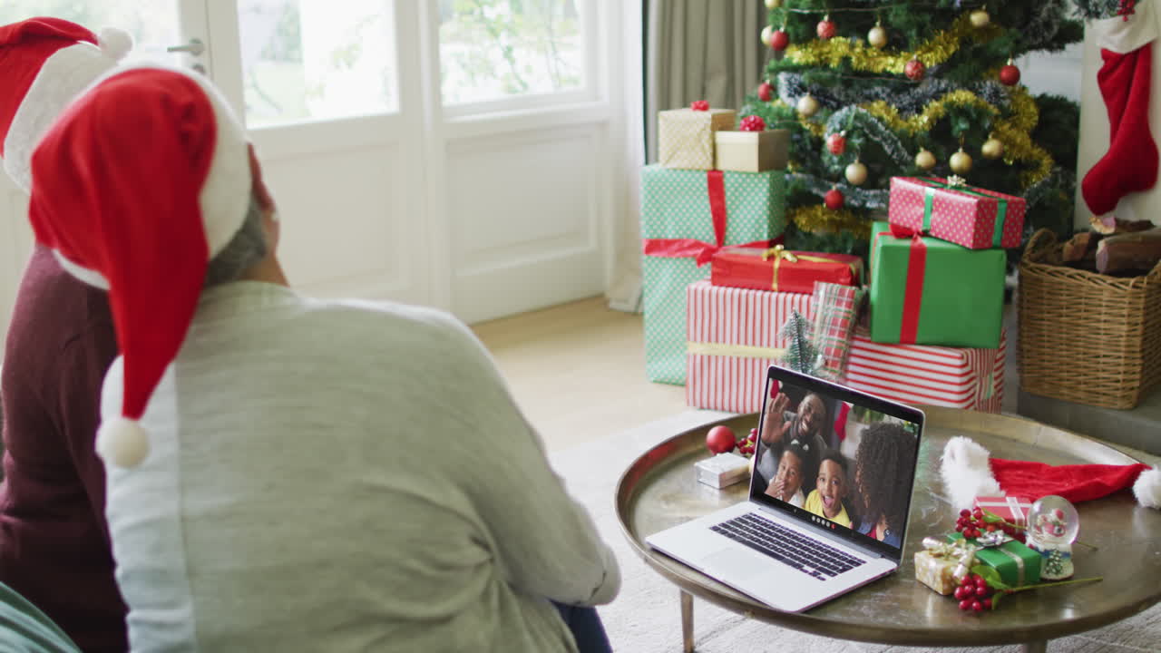 diversas amigas mayores que usan una computadora portátil para una videollamada de navidad con una familia sonriente en la pantalla