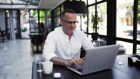 hombre de negocios sonriente trabajando en una computadora portátil en una cafetería. hombre profesional escribiendo en el teclado de la computadora portátil en el lugar de trabajo de la cafetería. retrato de hombre de negocios positivo mirando la pantalla de la computadora portátil en el interior