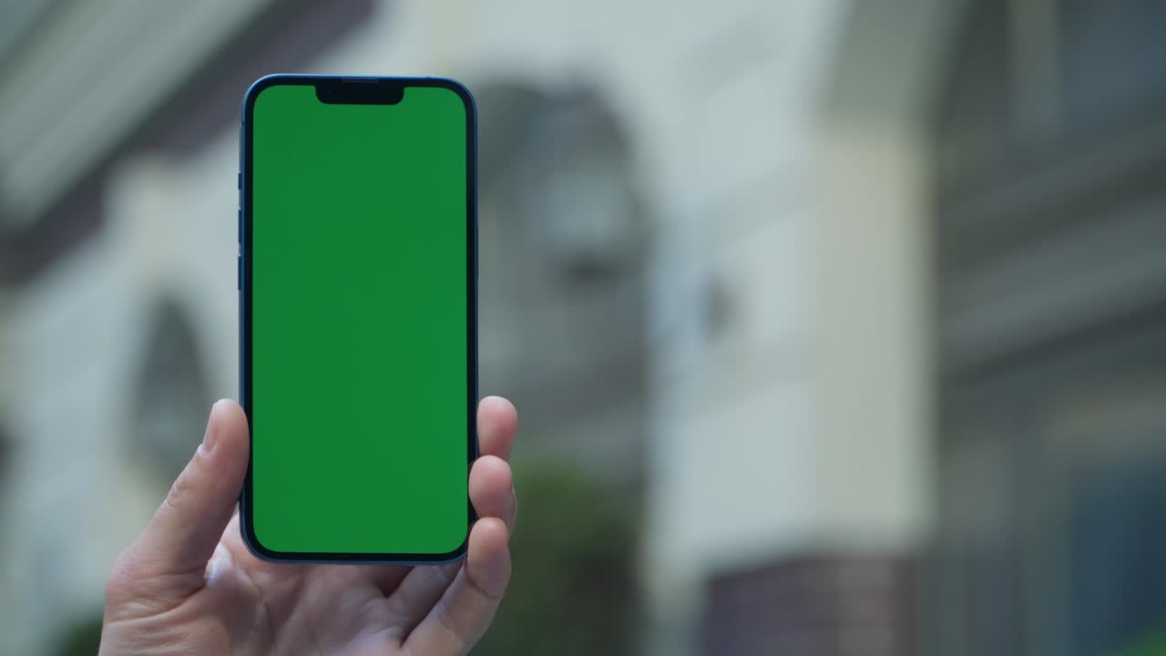 close-up de 4k de la mano de un hombre sosteniendo un teléfono inteligente con pantalla verde en una calle de la ciudad