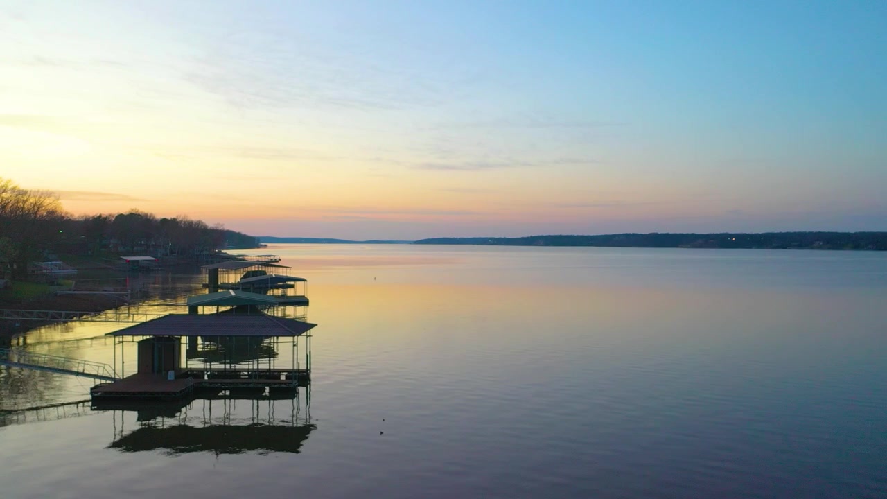 Vista drone del tranquillo lago Beaver con case sul lungolago, moli coperti per barche, insenature boscose, acque serali calme e un caldo bagliore del tramonto attraverso il panoramico paesaggio degli Ozarks dell'Arkansas