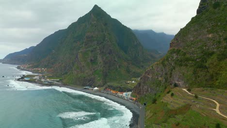 aerial view of mountains on madeira island with waves and coastline with buildings during cloudy day