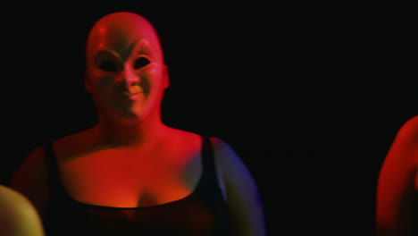 dolly across women in masquerade masks against black background