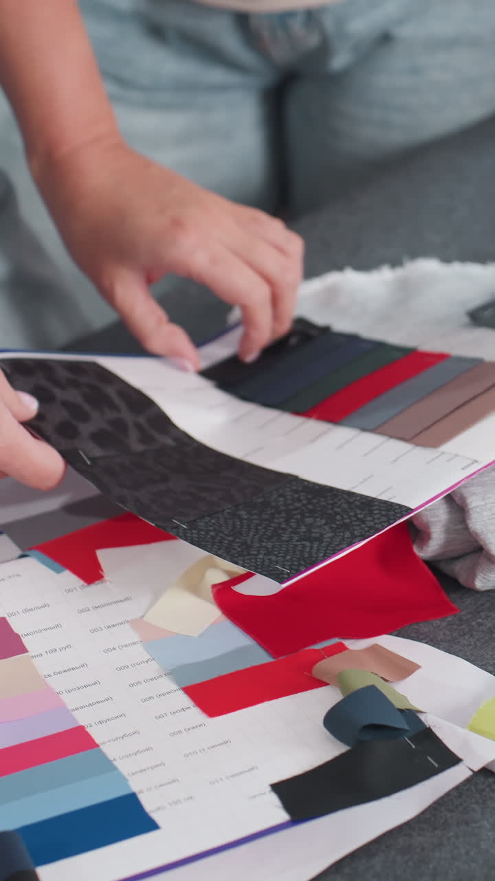 Unas manos colocan muestras de tela sobre una mesa; un estilista de interiores compara tiras de colores y muestras de tapicería texturizada; paleta de papel y tela vaquera cerca; primer plano de una selección cuidadosa; iluminación natural cálida.